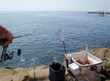 Sunny weather, rocky shore fishing scene. Hand holding rod, ground bait bucket and tackles set on the water edge. 磯際の釣り風景。釣人の竿、エサバッカンなど。
