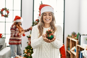 Poster - Woman couple holding xmas ball decorating christmas tree at home