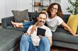 © Krakenimages.com - Middle age hispanic couple smiling happy and using touchpad. Sitting on the sofa with dogs at home.