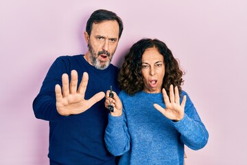 Sticker - Middle age couple of hispanic woman and man holding keys of new home doing stop gesture with hands palms, angry and frustration expression