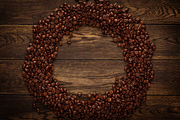 Wall Mural - Roasted coffee beans arranged into ring. Brown grains scattered in circle over dark wooden board background with empty space in middle. Round frame top view