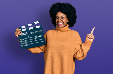 Poster - Young african american woman holding video film clapboard smiling happy pointing with hand and finger to the side