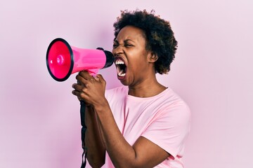 Wall Mural - African american woman with afro hair screaming with megaphone over pink background