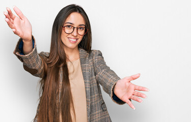 Canvas Print - Young hispanic girl wearing business clothes and glasses looking at the camera smiling with open arms for hug. cheerful expression embracing happiness.