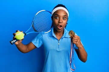 Wall Mural - African american woman with braided hair playing tennis holding racket and ball and winner medal afraid and shocked with surprise and amazed expression, fear and excited face.