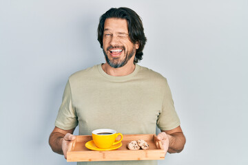 Sticker - Middle age caucasian man holding breakfast tray with cookies and coffee winking looking at the camera with sexy expression, cheerful and happy face.