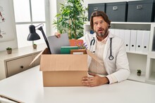 Handsome Middle Age Doctor Man Holding Box With Items In Shock Face, Looking Skeptical And Sarcastic, Surprised With Open Mouth