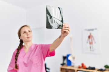 Canvas Print - Young caucasian woman wearing physiotherapist uniform holding xray at physiotherapy clinic