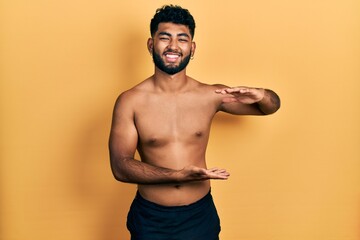 Poster - Arab man with beard wearing swimwear shirtless gesturing with hands showing big and large size sign, measure symbol. smiling looking at the camera. measuring concept.