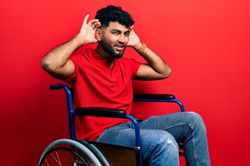 Canvas Print - Arab man with beard sitting on wheelchair trying to hear both hands on ear gesture, curious for gossip. hearing problem, deaf