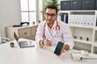 © Krakenimages.com - Young hispanic man wearing doctor uniform showing medical smartphone app at clinic