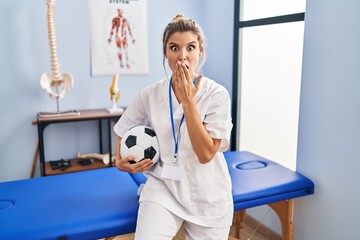 Poster - Young woman working at football therapy clinic covering mouth with hand, shocked and afraid for mistake. surprised expression