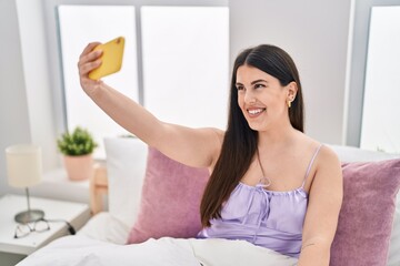 Canvas Print - Young hispanic woman make selfie by smartphone sitting on bed at bedroom