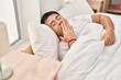 Young chinese man lying on bed yawning at bedroom