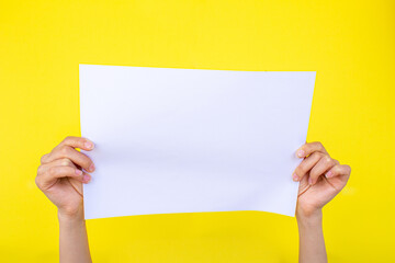 Hand holding blank paper isolated on yellow background.