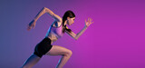 Fototapeta Londyn - One young muscular girl, female runner or jogger training isolated on pink-blue background in neon light. Sport, track-and-field athletics, competition and active lifestyle concept