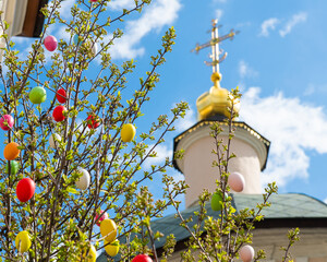 Colorful easter eggs on the tree near the church in sunny spring 