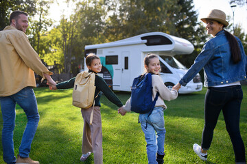 Wall Mural - Rear view of young family with backpacks going to caravan outdoors at park.