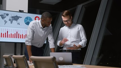 Poster - Two young men discussing business strategy using a tablet in a modern office building