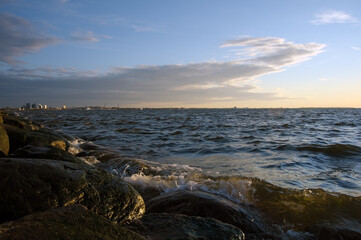 Sea with wave splashing into rocks on sunset background sky