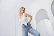 Young Woman In White Bodysuit And Jeans Standing In Living Room.