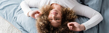 Top View Of Pleased Woman With Curly Hair Stretching On Bed At Home, Banner.