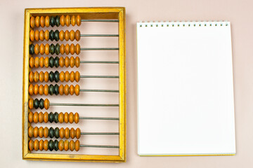 old antique wooden abacus and a notebook (notebook) with a blank page for writing on a beige backgro