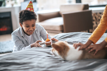 Wall Mural - A boy smiling and offering a pancake with a candle to the puppy