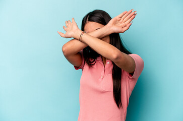 Young hispanic woman isolated on blue background keeping two arms crossed, denial concept.