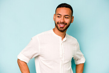 Wall Mural - Young hispanic man isolated on blue background laughs happily and has fun keeping hands on stomach.