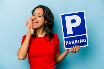 Wall Mural - Young hispanic woman holding parking placard isolated on blue background shouting and holding palm near opened mouth.