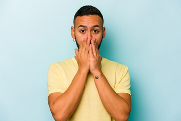 Wall Mural - Young hispanic man isolated on blue background shocked, covering mouth with hands, anxious to discover something new.