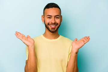 Young hispanic man isolated on blue background makes scale with arms, feels happy and confident.