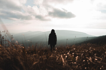 Young woman standing on grassy field on a windy evening in autumn mountains enjoying view of nature. Majestic sunset over mountains. Czech republic, Jeseniky