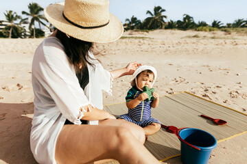 Wall Mural - Mother and her baby son playing on the beach during summer vacation