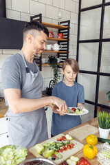 Wall Mural - Handsome father and his teenager son spending quality time together. Men doing chores, cooking healthy vegetable salad, tasty food in the kitchen at home