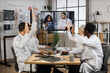 © sofiko14 - Team of multiethnic healthcare doctors sitting at table with arms raised during online video meeting. Medical workers in white lab coats voting for new successful tomographic project in modern clinic.