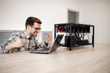 Programmer working on his cryptocurrency mining rig checking bitcoin value and earnings feeling happy.