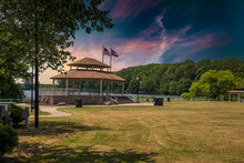 A Brown Wood And Stone Pergola In The Park Surrounded By Lush Green Trees, Grass And Plants And The Blue Waters Of Lake Acworth With Powerful Clouds At Sunset At Cauble Park In Acworth Georgia USA