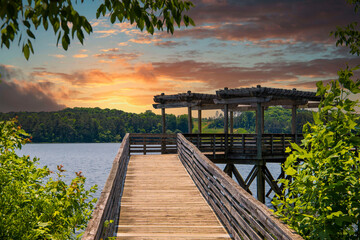 a brown wooden bridge over the silky green waters of Lake Acworth surrounded by lush green trees and plants with powerful clouds at sunset at Cauble Park in Acworth Georgia USA