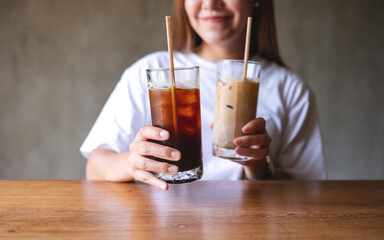 Wall Mural - Closeup image of a young woman holding and drinking two glasses of iced coffee