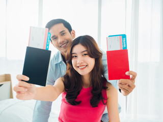 Couple travelers in happy holiday. Summer vacation honeymoon concept. Smiling Asian couple holding and showing passport, ready to trip, young woman and man on white curtain at home background.