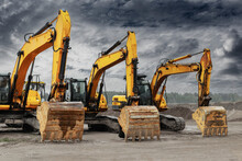 Powerful Excavators At A Construction Site Against A Blue Cloudy Sky. Earthmoving Construction Equipment. Lots Of Excavators.