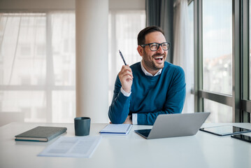 Excited businessman with laptop looking away while working at office desk