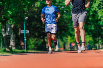 Wall Mural - Two healthy young men running in the park on a sunny day..