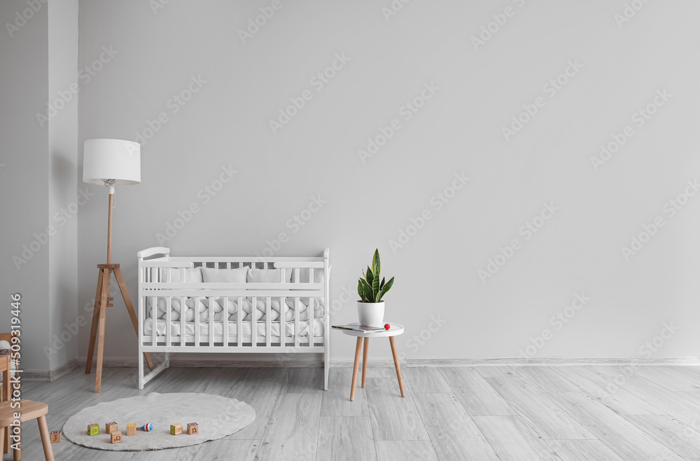 Interior of light nursery with baby crib, lamp and table