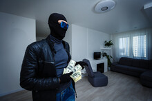Robber Man Dressed In Black Hoodie Stands With Disguised Face And Holds A Lot Of Money In His Hands, Stole A Large Amount, A Thief Man Stole A TV