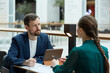 Portrait of bearded businessman listening to young woman during meeting at cafe table with documents
