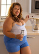 Strahlende, übergewichtige Frau mittleren Alters mit großer Oberweite und langen, brünetten Haaren bereitet Kaffee in einer einfachen Küche zu