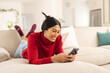 © Wavebreak Media - Smiling biracial young woman using smart phone while lying on sofa at home